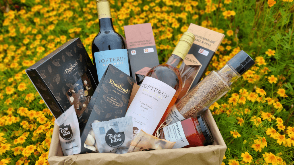 En gavekurv med specialiteter fra gårdbutikken Tinnetgaard ligger på en blomstereng
