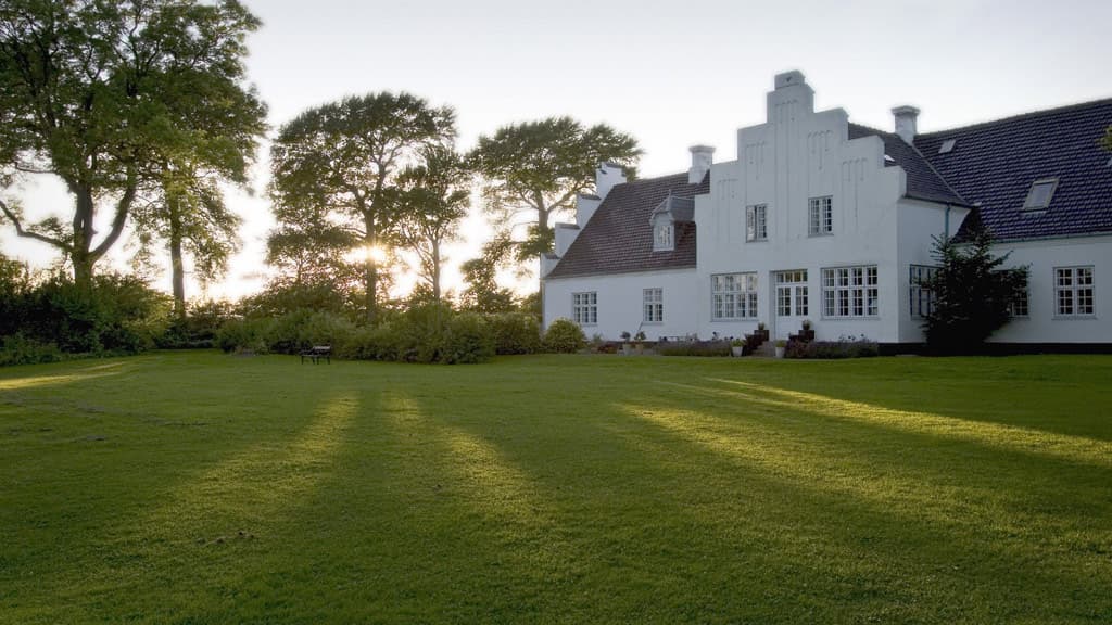 Brandbjerg Herregårds facade med lysindfald ved træerne på flot nyslået grøn plæne