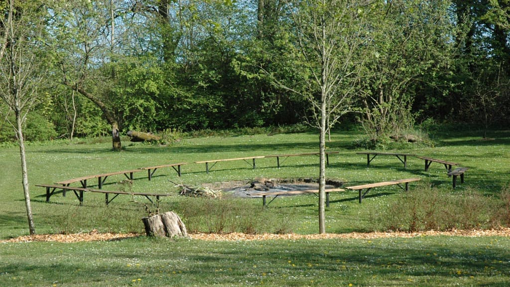 Bålplads med bænke i grønne omgivelser og træer omkring