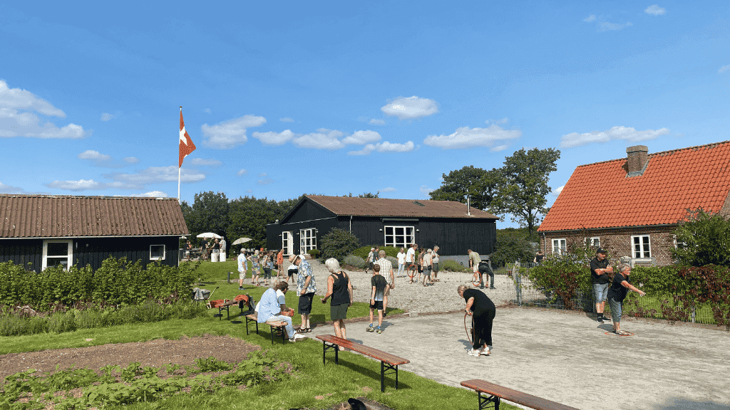 Udeområde med to sorte træbygninger og en rød murstensbygning