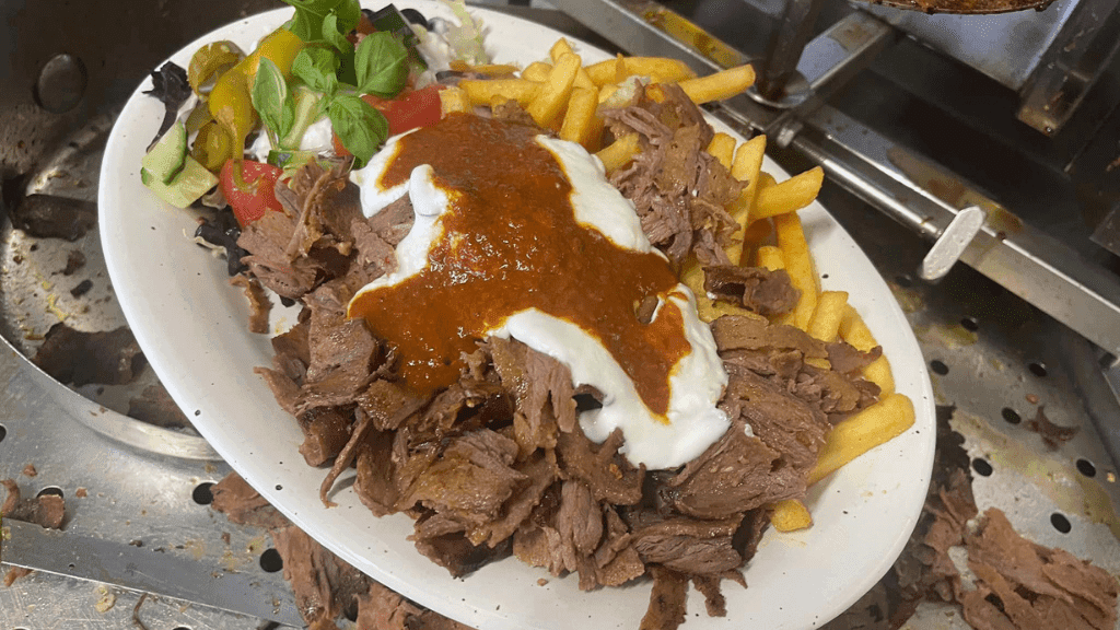 Tallerken med blandet salat, kebab, pommes frites og hvid og rød dressing